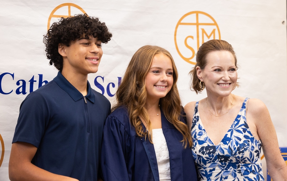 8th grade graduate posing for photo with family in front of STM Step-and-Repeat
