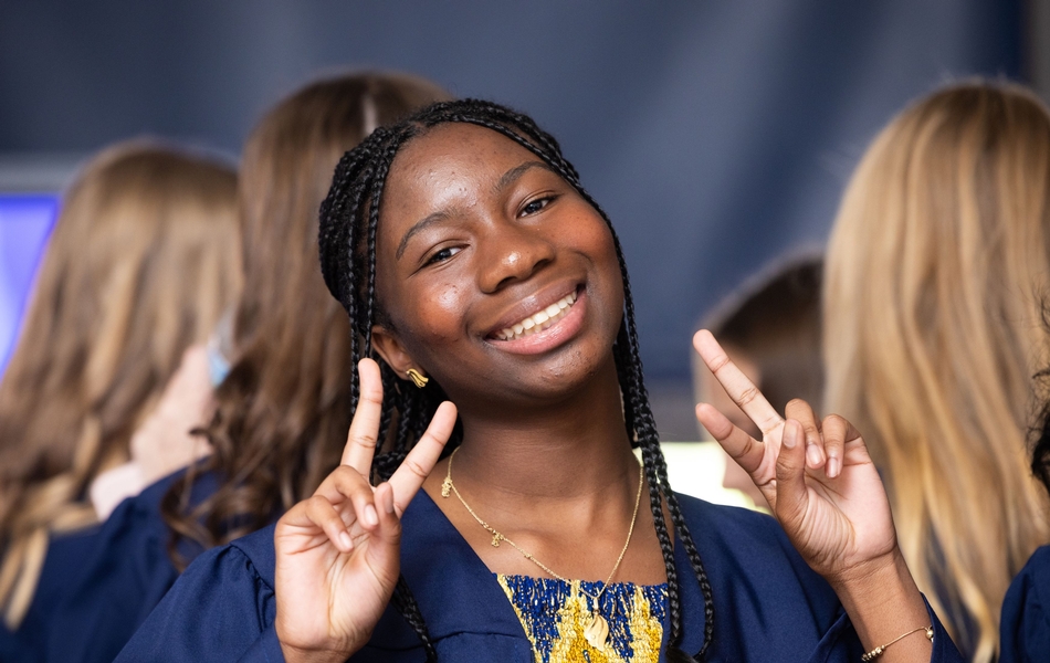 8th grade graduate in blue gown giving two peace signs
